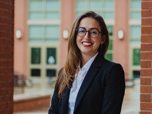 A photo of Ava Fergerson, dressed in a collared shirt and blazer with red lipstick. She is smiling at the camera. 