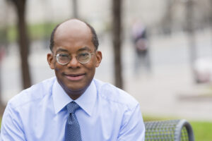 A photo of Dr. Ferguson dressed in a suit and tie and seated outside. He is smiling at the camera. 